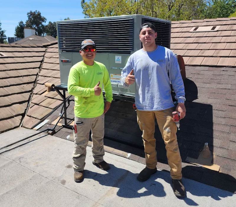 Two certified HVAC technicians giving a thumbs-up on a roof next to a newly serviced Trane ac repair in Kingsburg