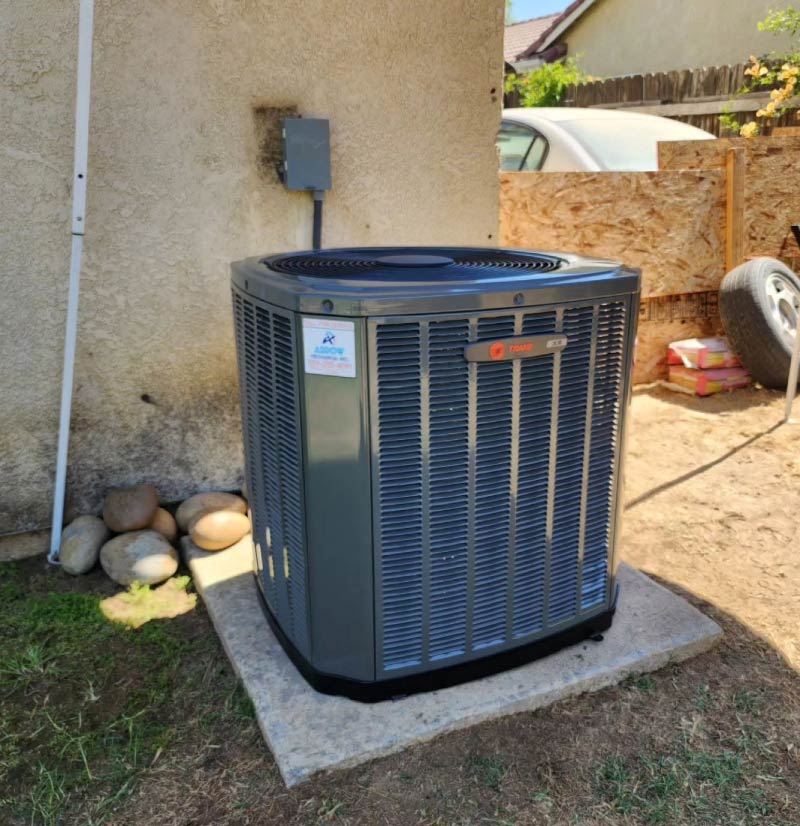 A brand new grey Trane XR outdoor air conditioner condenser unit installed on a concrete pad next to a residential stucco wall.