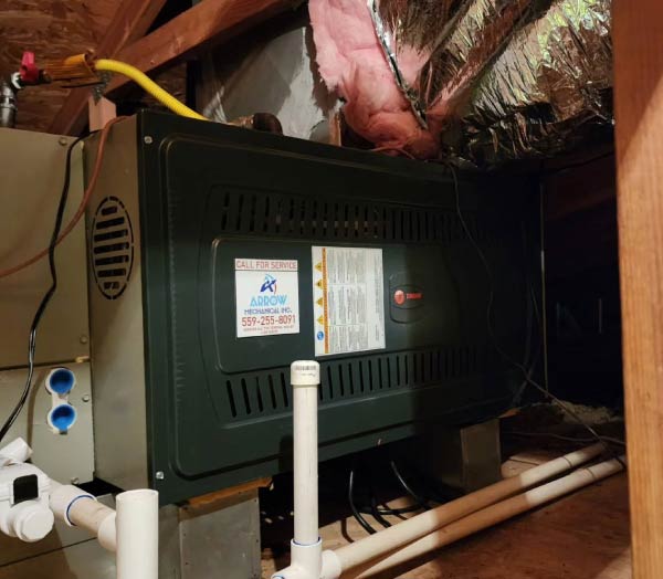 An attic installation featuring a Trane heating and cooling unit connected to flexible insulated ductwork and PVC drainage pipes