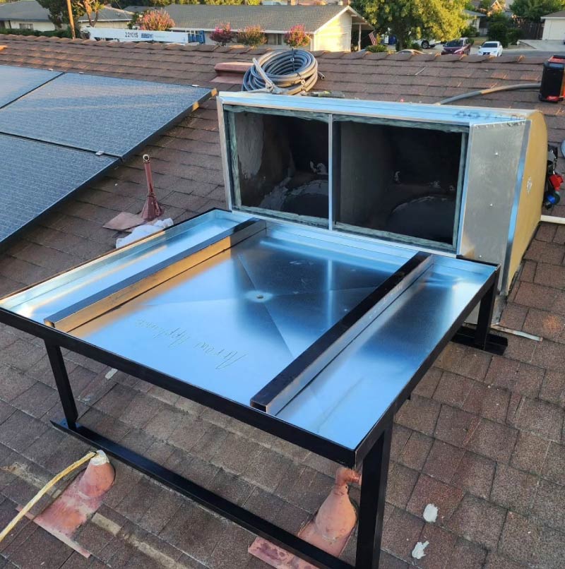 A rooftop HVAC installation in progress on a shingled roof, showing a new sheet metal curb adapter base etched with Arrow Appliance next to a solar panel array.