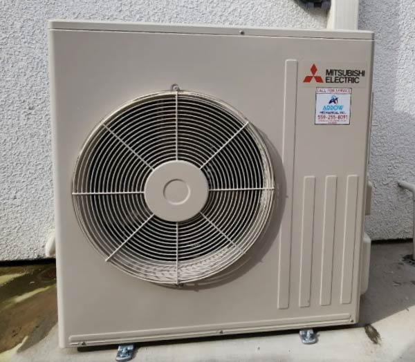 A compact Mitsubishi Electric outdoor mini-split heat pump unit installed against a stucco wall with an Arrow HVAC service sticker.