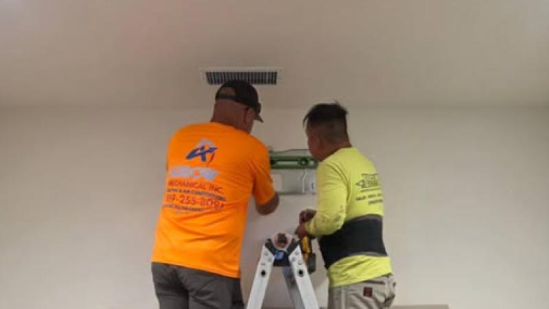 Two HVAC ac services technicians from Arrow Mechanical installing a ductless mini-split wall bracket inside a home