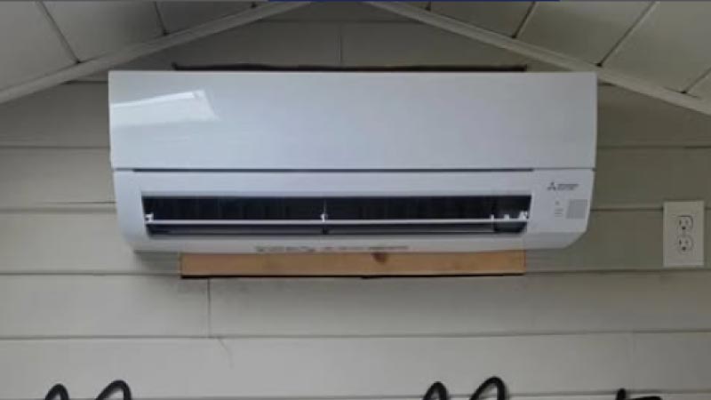 White Mitsubishi Electric mini-split AC indoor unit mounted cleanly on a light-colored wood paneled wall.