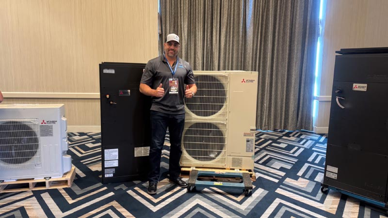 Arrow HVAC technician giving a thumbs up while standing next to premium Mitsubishi Electric heating and cooling systems.
