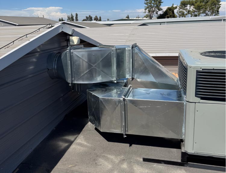 Finished installation of shiny galvanized sheet metal rectangular ductwork connecting a packaged rooftop HVAC unit to a metal building wall