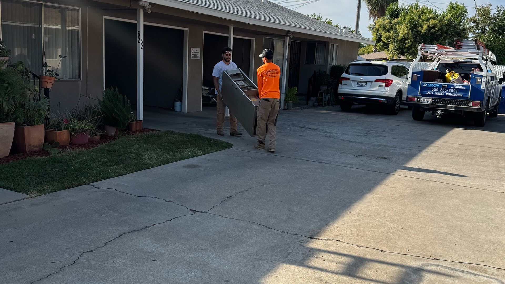 Two Arrow HVAC technicians carrying a new furnace unit across a driveway for a residential installation service