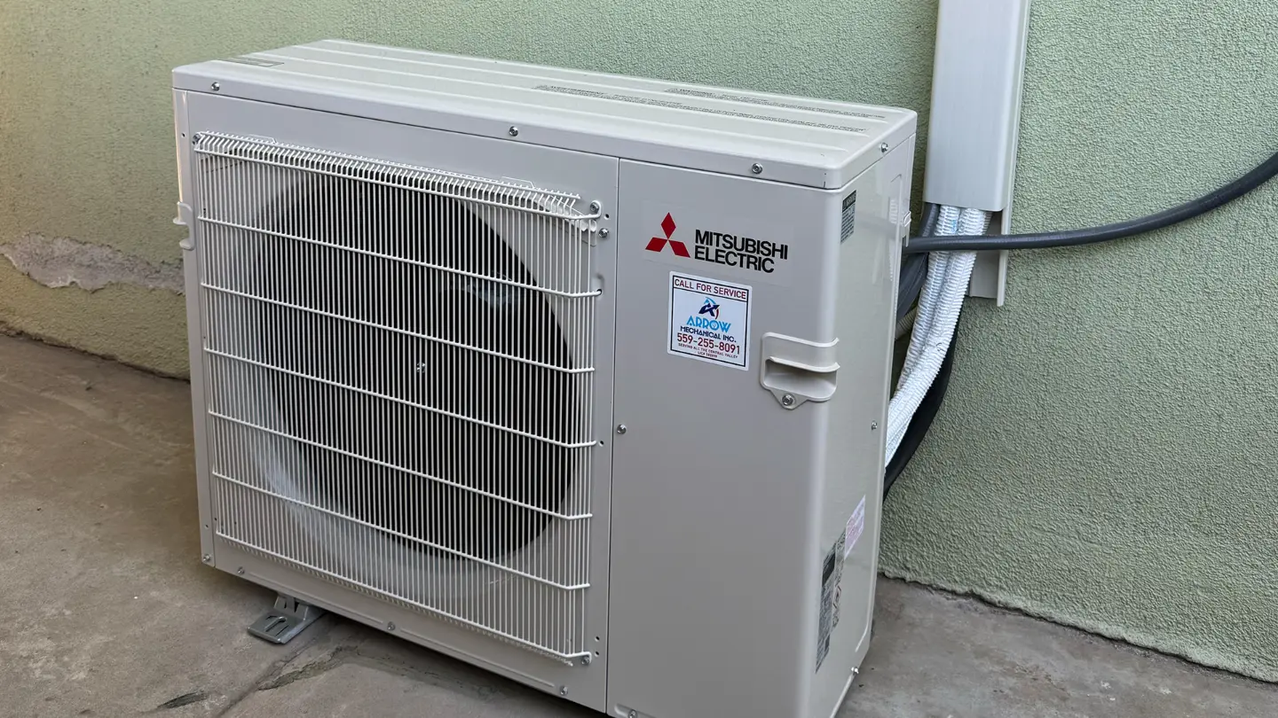 Outdoor Mitsubishi Electric mini-split heat pump unit with an Arrow Mechanical service sticker installed against an exterior stucco wall.
